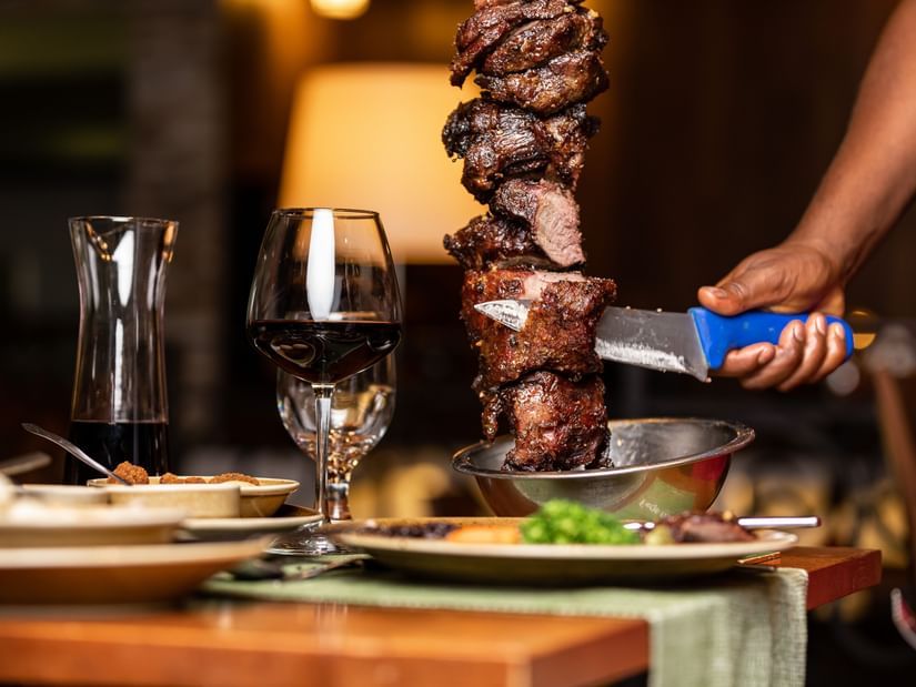 A close up of a staff slicing meat on a skewer on the table inside a restaurant - Ramada by Wyndham Addis, Addis Ababa.