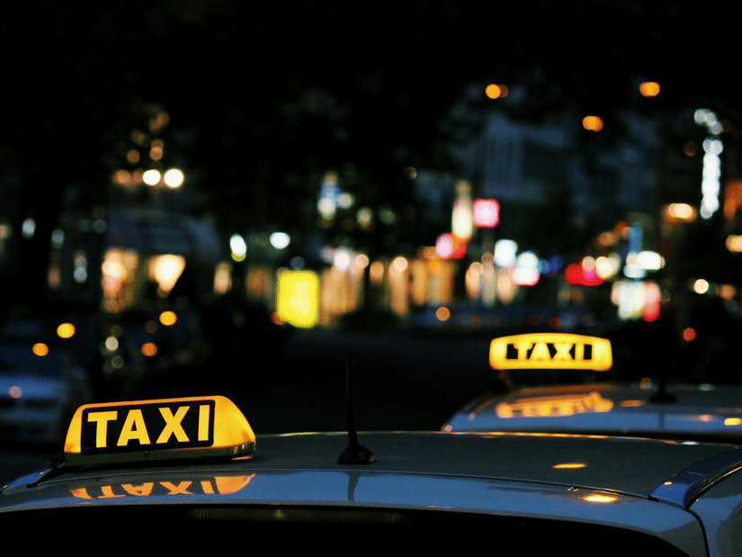 A close up of a taxi sign board on top of a car which is highlighted, signifying to be hired.