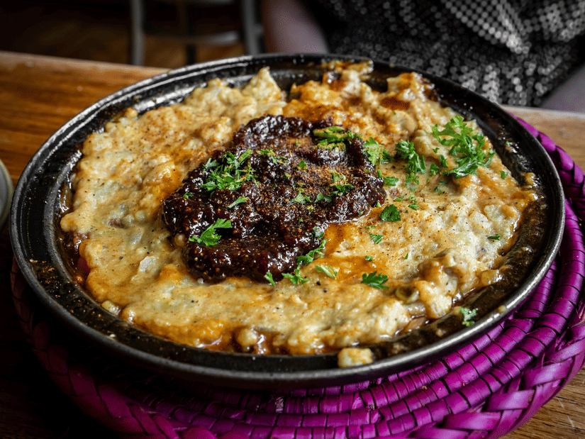 A bowl containing pan fried lamb with potato/cheese kept below it, a part of authentic Ehiopian cuisine