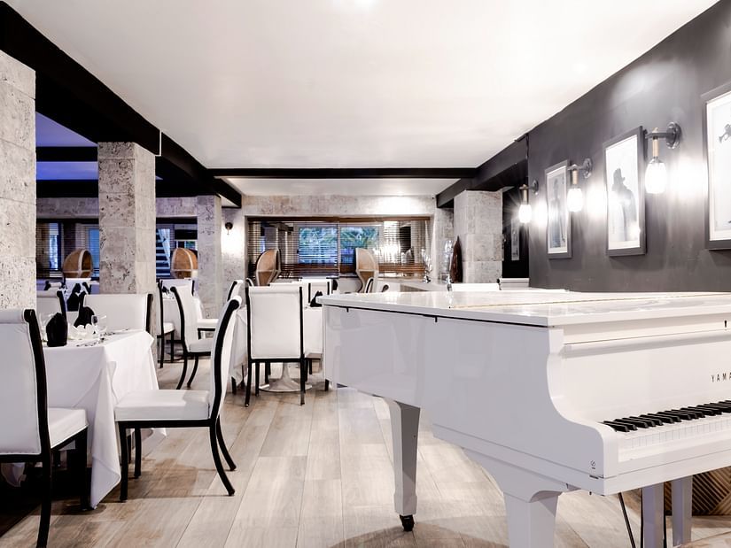 An image of a white piano and upholstered chairs in our Rocksteady Restaurant in Montego - S Hotel Montego Bay, Jamaica