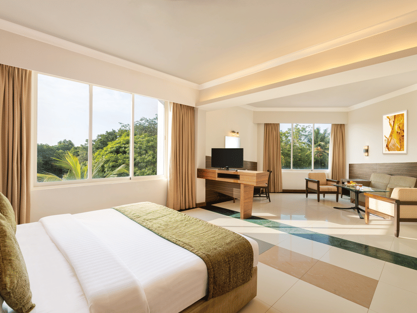 A double bed and a living area opposite it with a tv and sofas inside the Deluxe Room at Sangam Hotel, Thanjavur - Thanjavur Hotel Rooms