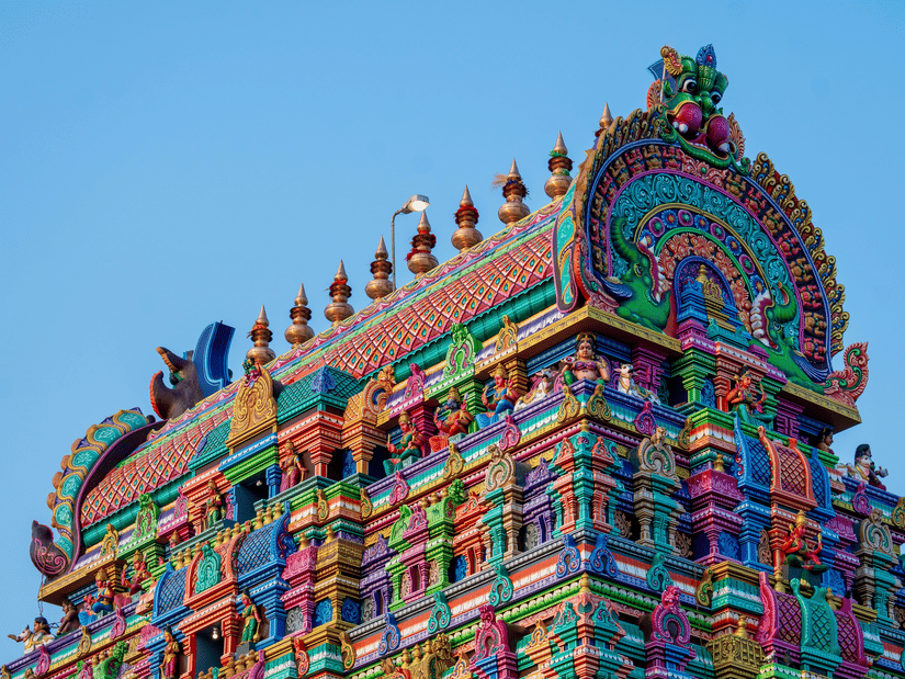 A close up view of Pillayarpatti Karpaga Vinayagar's gopuram with intricate carvings of numerous deities on it and blue sky in the background.