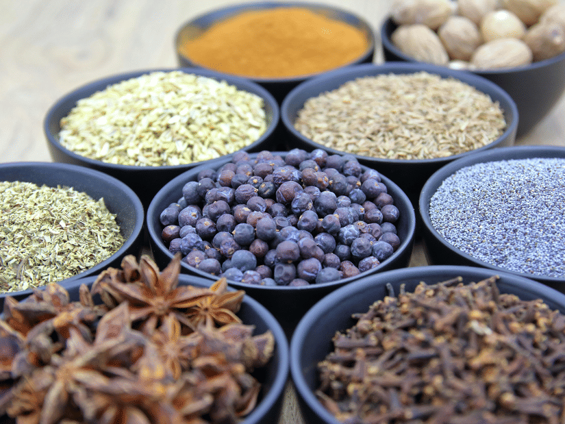 Assorted whole spices arranged in small bowls, including peppercorns, cloves, and lentils
