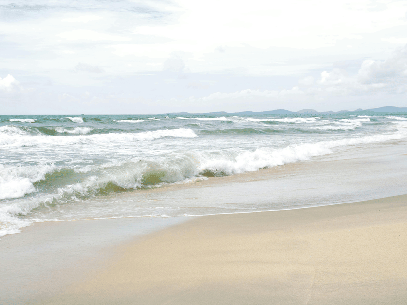 Turquoise ocean waves gently rolling onto a sandy tropical beach with distant mountains on the horizon