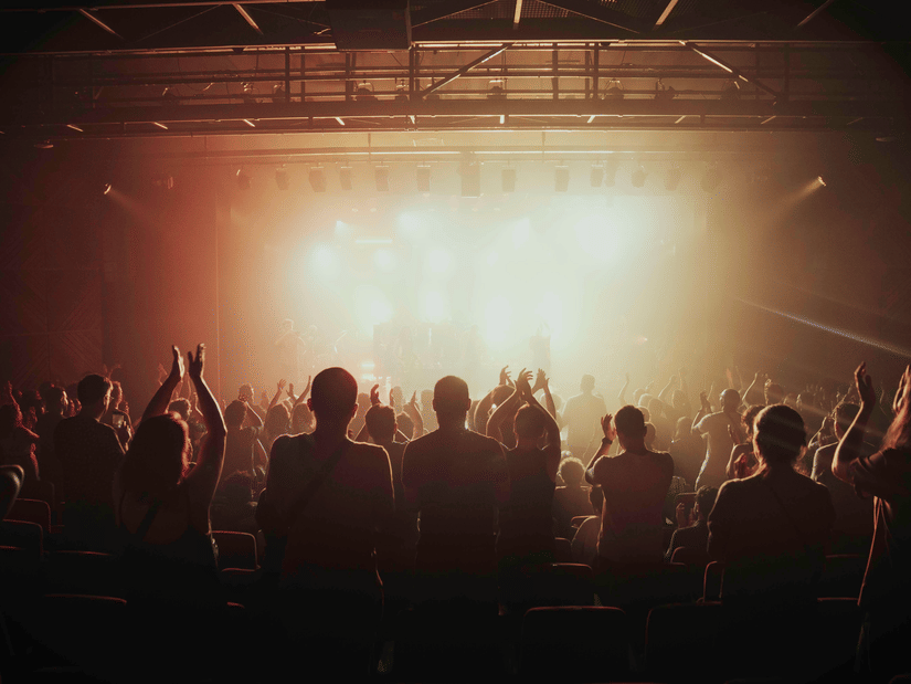 Crowd gathered before a brightly lit stage during a live music performance with an energetic festival atmosphere