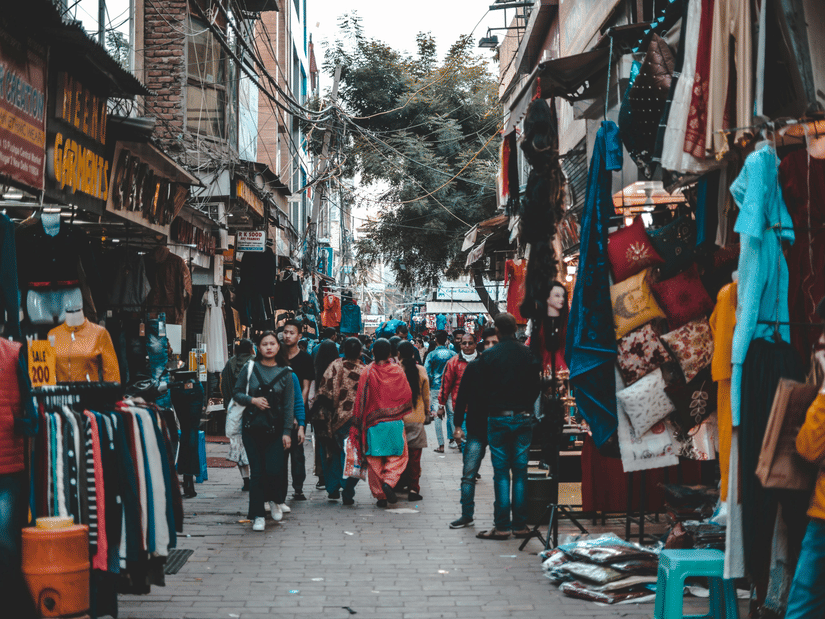 An overview of a crowded market street with people shopping and stalls on either side.