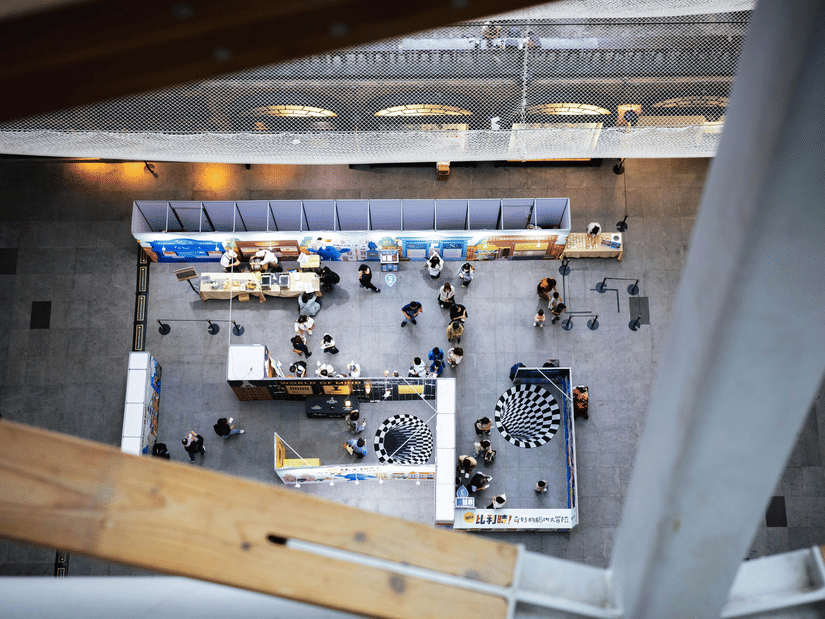 A top-down view of a trade show with different booths, showcasing their products, and people flocking towards them.