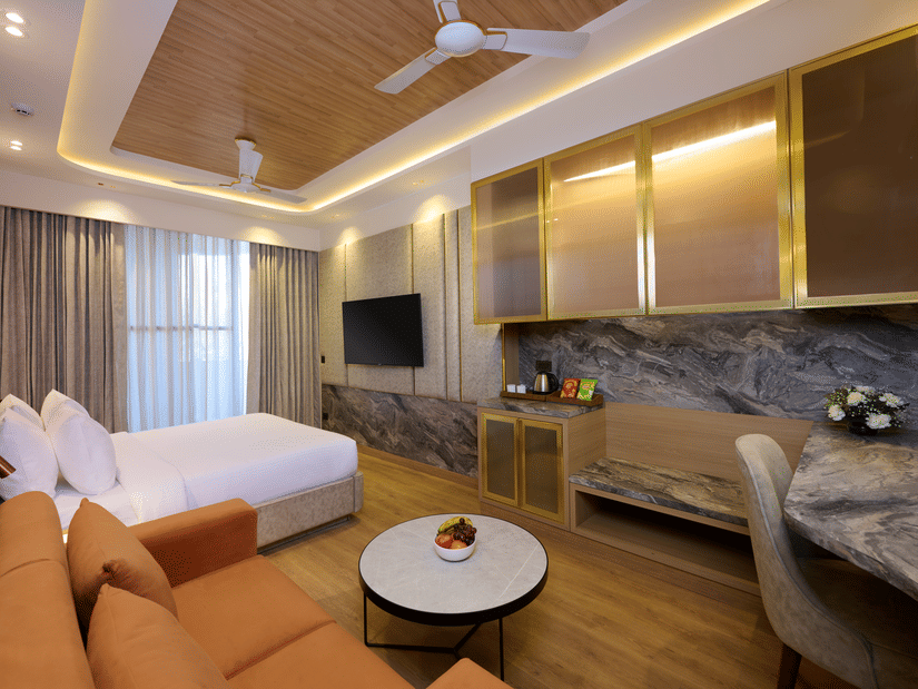 Living area and bedroom combo at Tulip Inn Gurugram with a marble-topped coffee table, a couch, and integrated storage units.