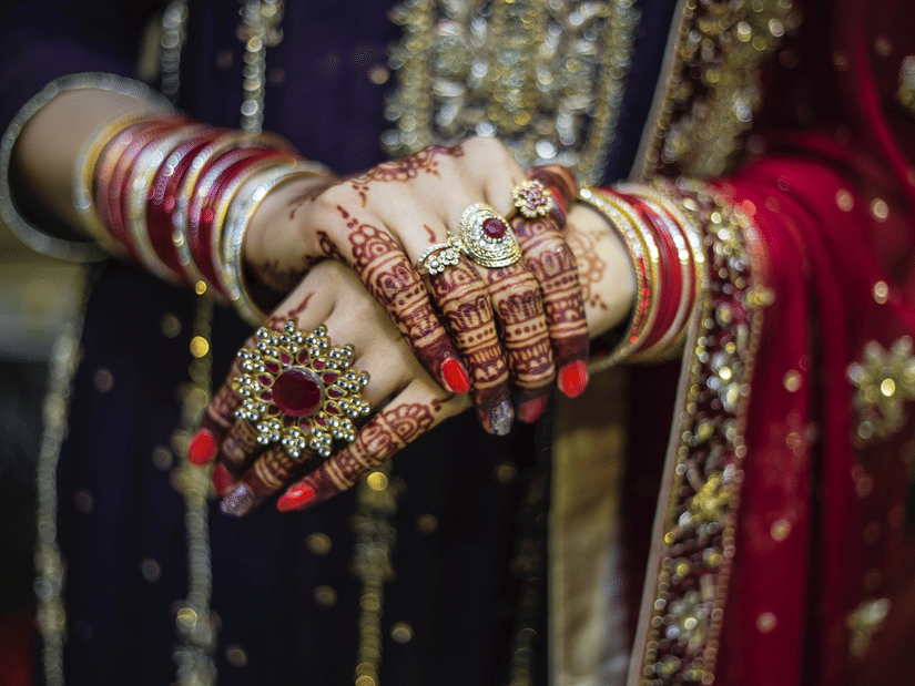 A close-up of bridal mehendi on hands with gold jewellery.