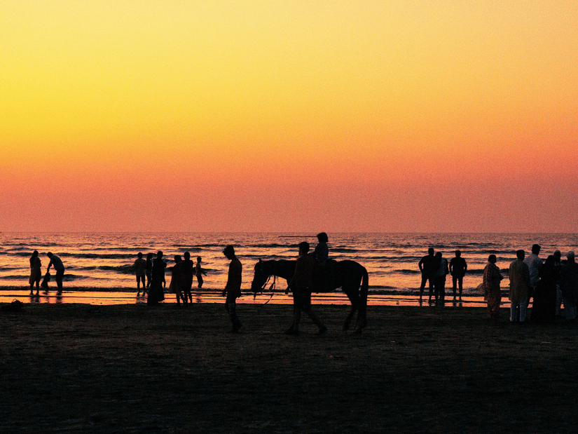 Visitors enjoying an evening at Daman Beach as the sun sets over the Arabian Sea, with silhouettes of people and a horse ride along the shoreline