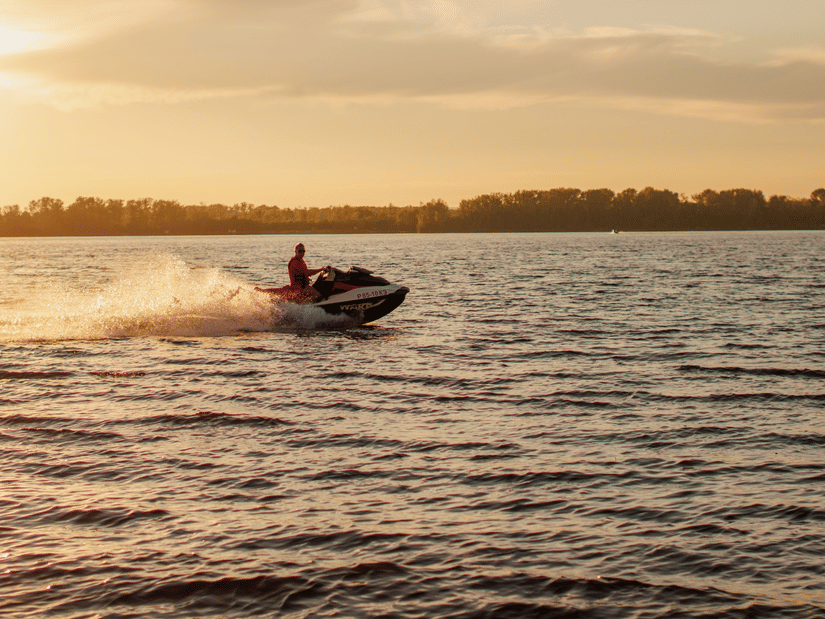 Person riding a jet ski across calm waters during a golden sunset.