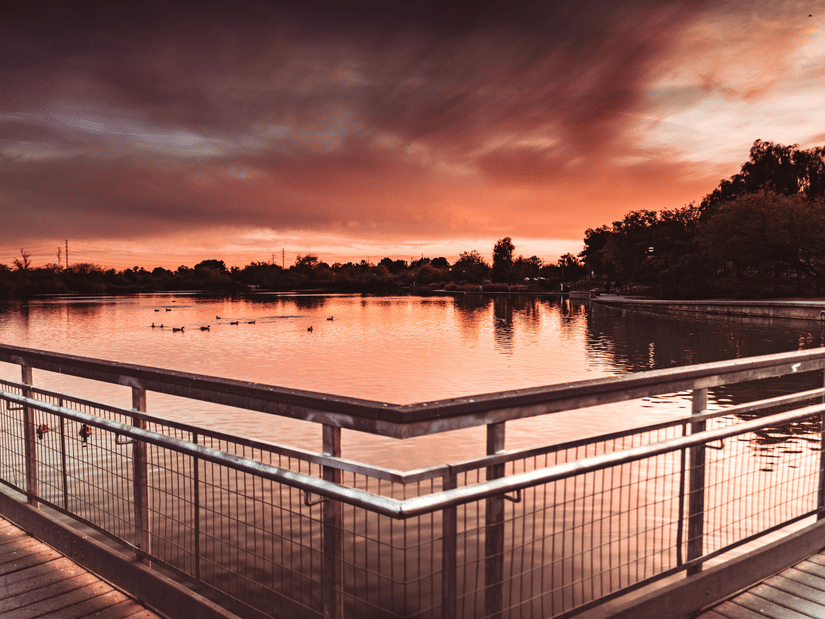 A view of a lake after a sunset with different hues in the sky, with trees in the distance.