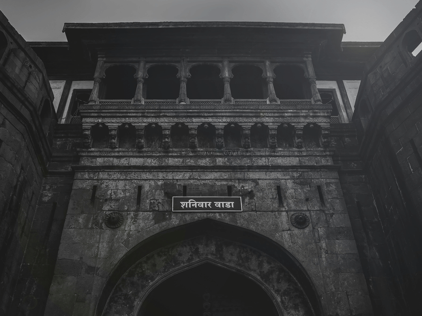 A stone gateway structure with arched opening, carved details, and dark exterior under cloudy sky.