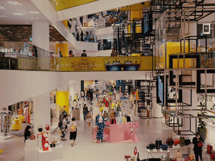 An interior of shopping mall with multiple floors, escalators, stores, seating areas, and people walking through the space.