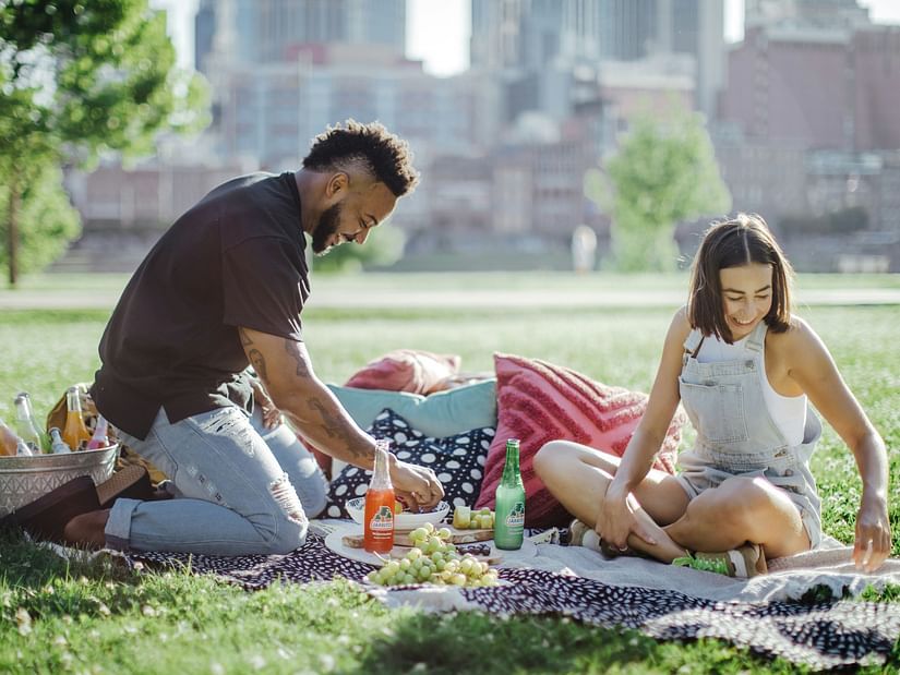 A couple sitting in a park with manicured grass enjoying a picnic.