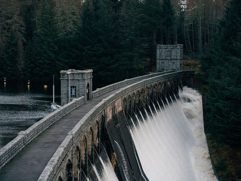 Dam gate with water flowing on one side and still water on the other side with greenery in the distance.