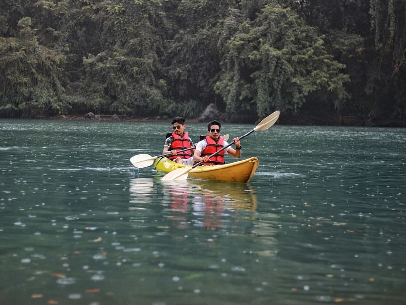 two people boating in a yellow boat over a water body with green forest in the background.