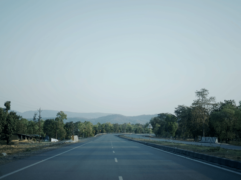 Wide highway cutting through a forested landscape with distant hills in the background.