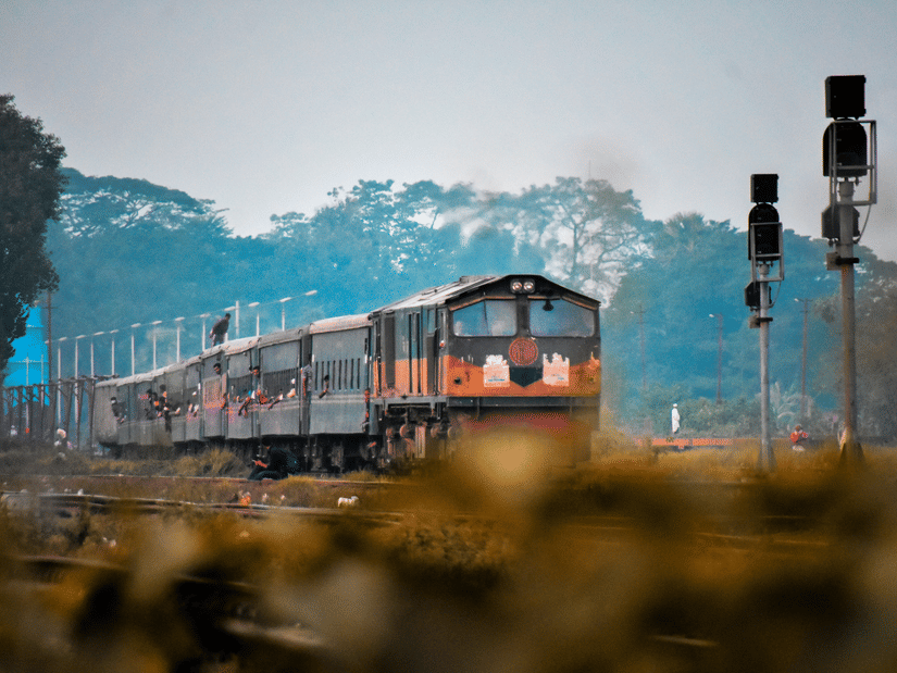 A train running on railway tracks with two signals and trees in the background