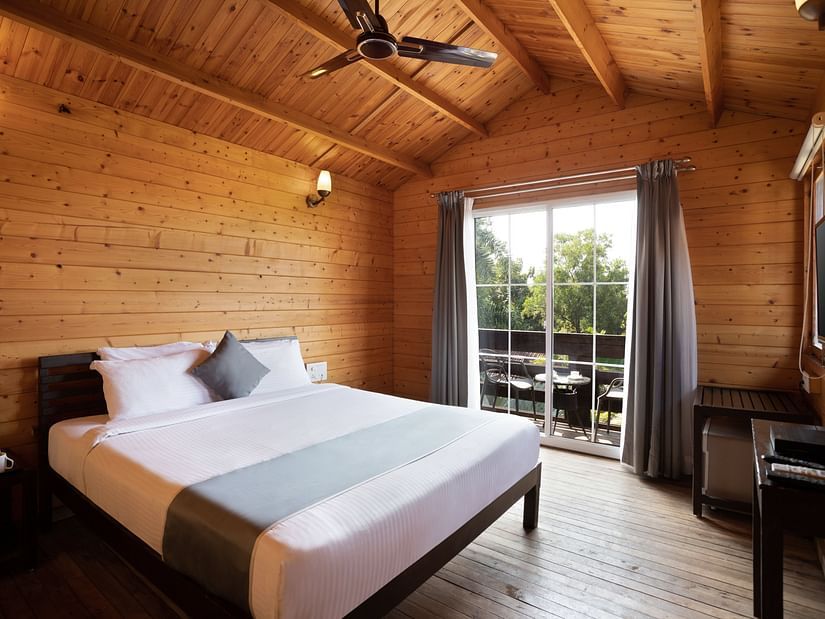 The interiors of the wooden cottage room features a large bed, a full length window and wooden walls