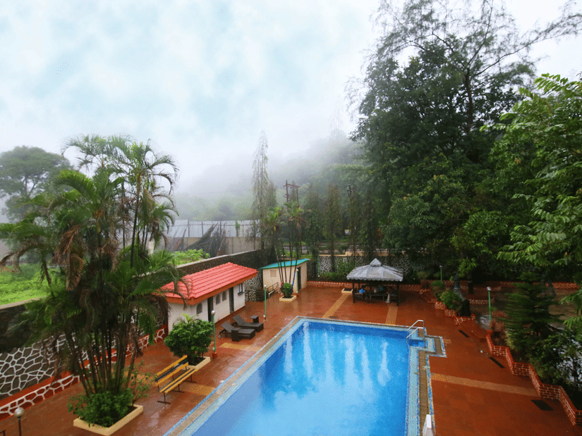 A tranquil swimming pool sits at the heart of a lush garden with mist lingering among the trees | Zara's Resort