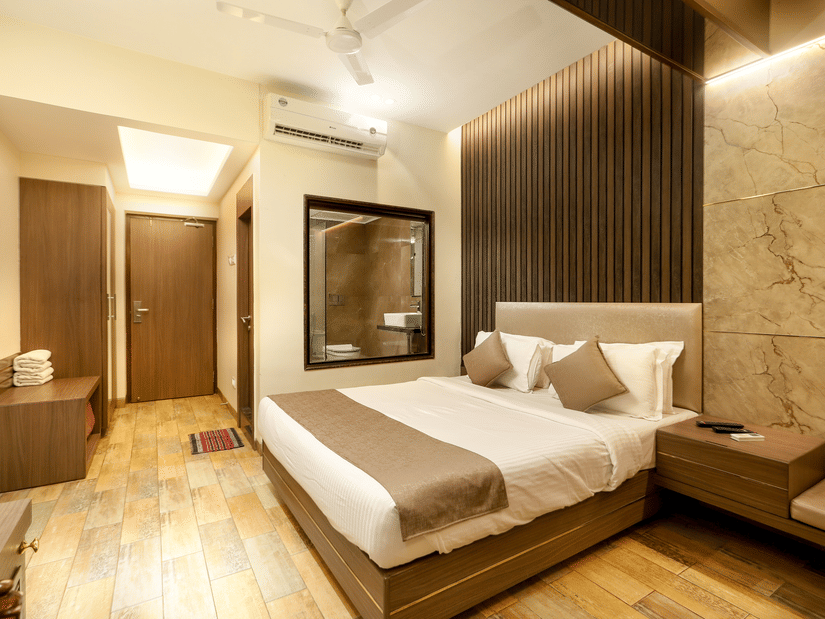 A neatly made bed  in our Deluxe Room rests against a wooden panel wall, lit by warm ceiling lights, with clean lines and minimal furnishings | Zara's Resort