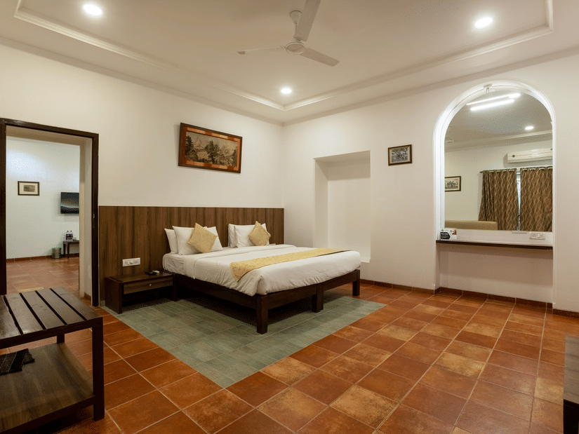 The interconnecting room at Zara's Resort, Khandala, featuring a plush bed set against a wooden panel wall, with warm lighting, and a connecting doorway leading into an adjoining room.
