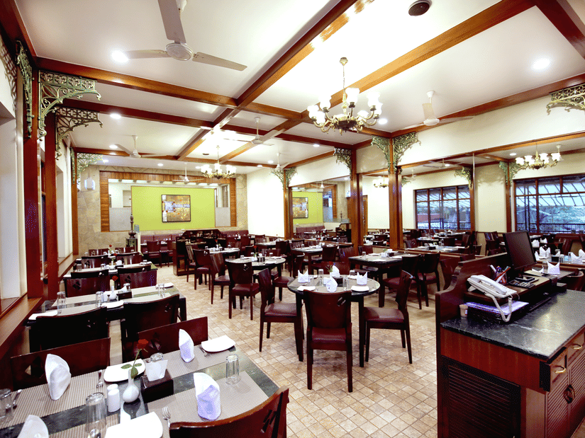 Spacious restaurant at Zara's Resort, Khandala, featuring a well-lit dining hall with neatly set tables and a chandelier, creating a warm, and inviting space for meals.