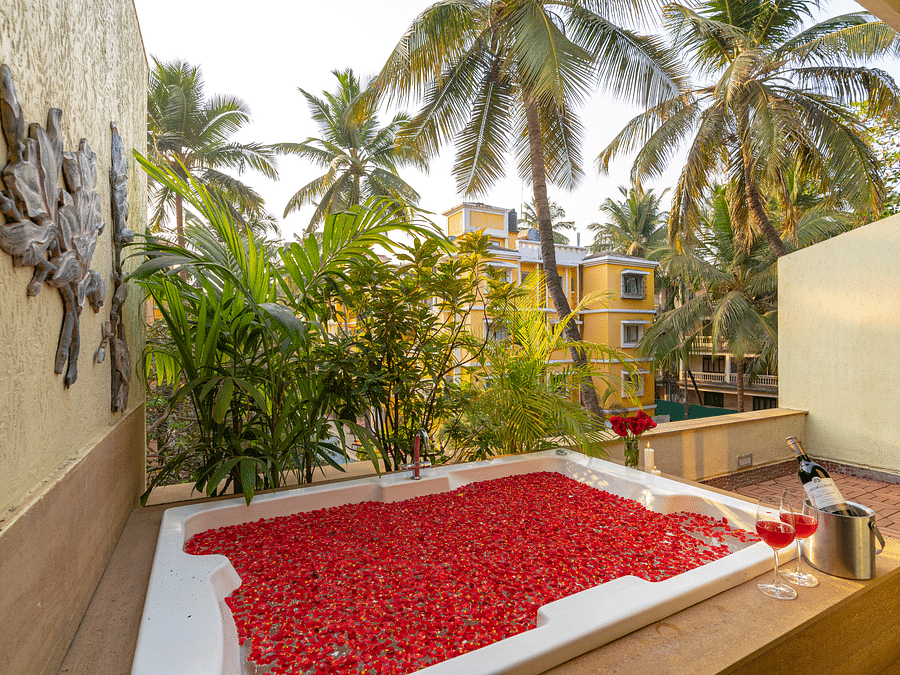 An image of an outdoor bathtub filled with rose petals and water, overlooking palm trees.
