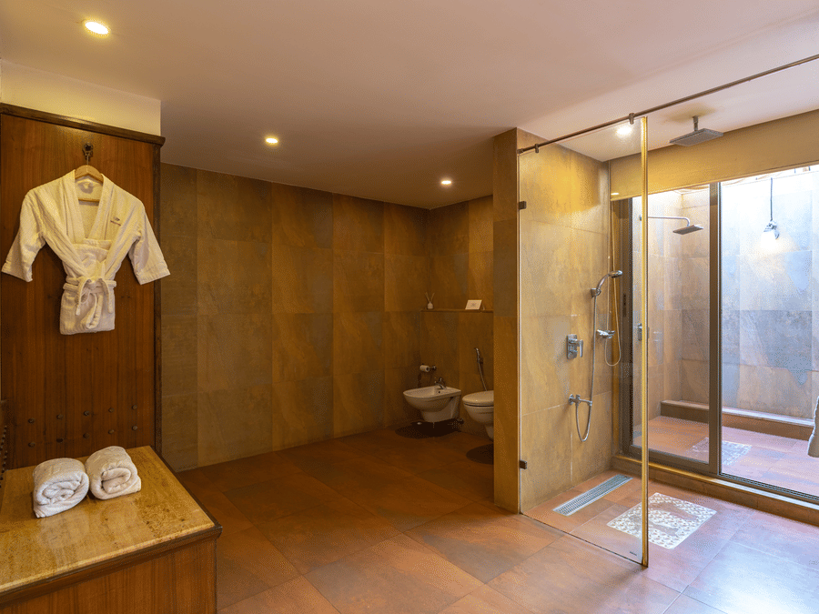 A washroom featuring a western toilet, bathrobe, towels, and an indoor and outdoor shower area separated by a glass window.