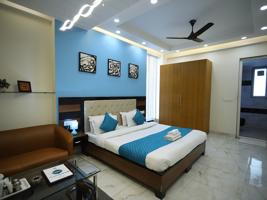 A hotel room featuring a made bed with pillows, a sofa with a table, a closet, and wall decorations - Asian Suites Cyber Park, Gurgaon.