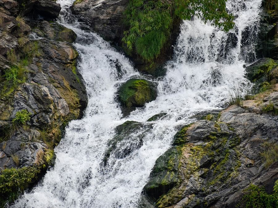 A close-up shot of a waterfall cascading over dark, moss-covered rocks.