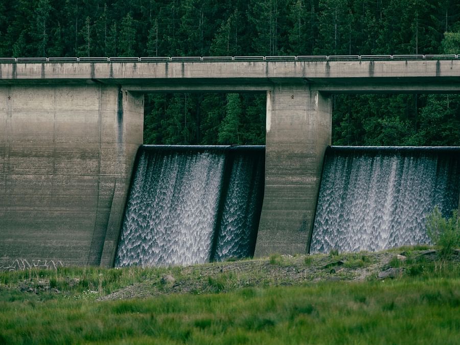 Image of a dam with water running down it and green grassland around.