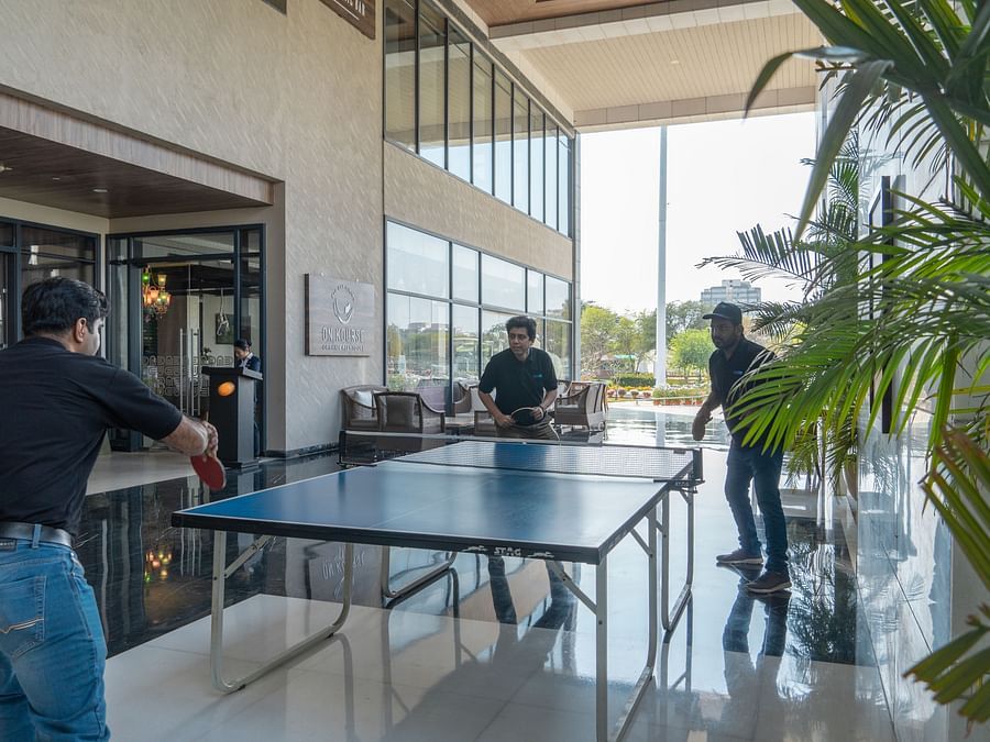 Three people playing table tennis in a modern indoor area.