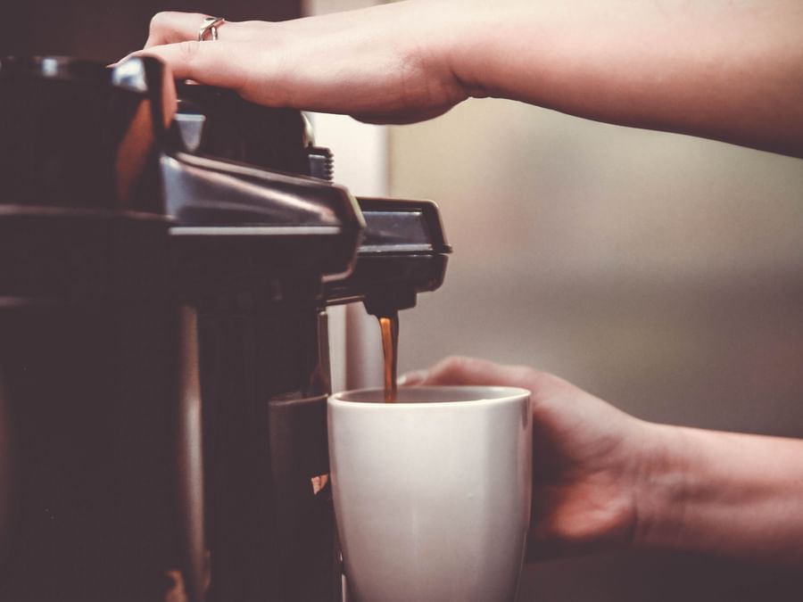 A zoom shot of a person pressing the coffee machine's button as the coffee pours into a white mug that the person holds