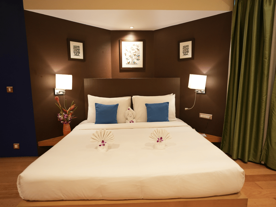 Suite room at The Beatle Hotel, Powai featuring a double size bed, with bedside table with lamps on either side, and a huge curtain on one side.