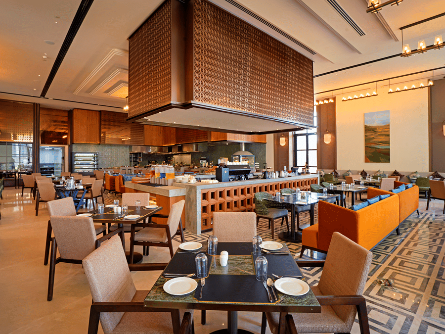 View of CHITHIRAI restaurant at The Residency Signature Madurai with a buffet counter, orange accents, wooden ceiling, and warm ambient lighting.