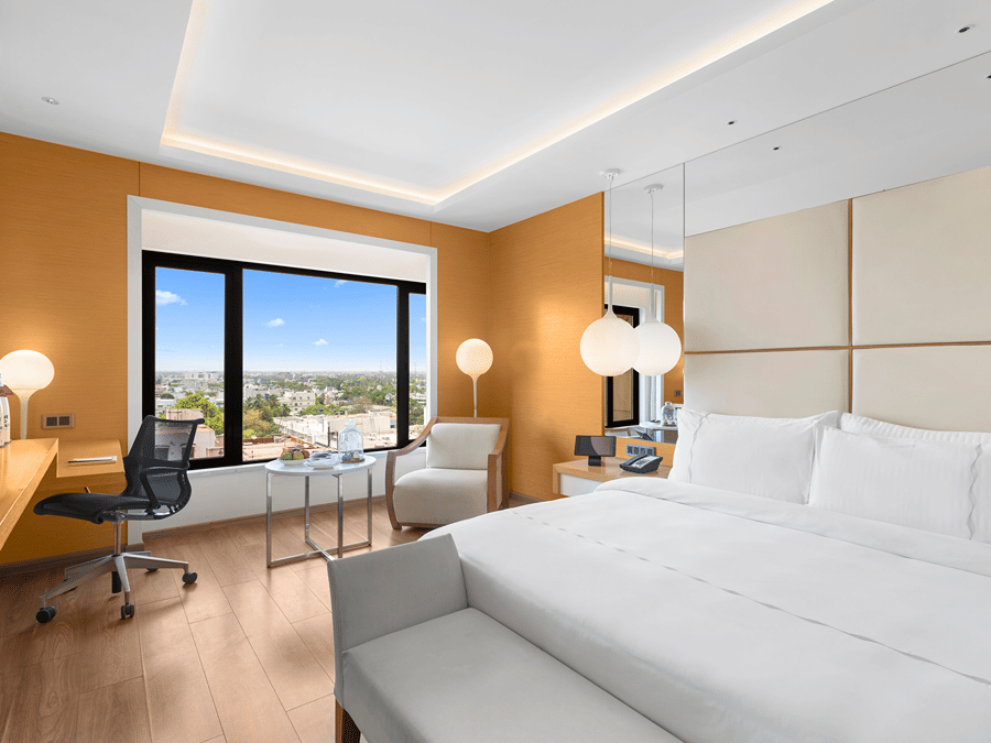Club Room with a spacious cozy bed, corner chair, and a view from the window at The Residency Towers Coimbatore