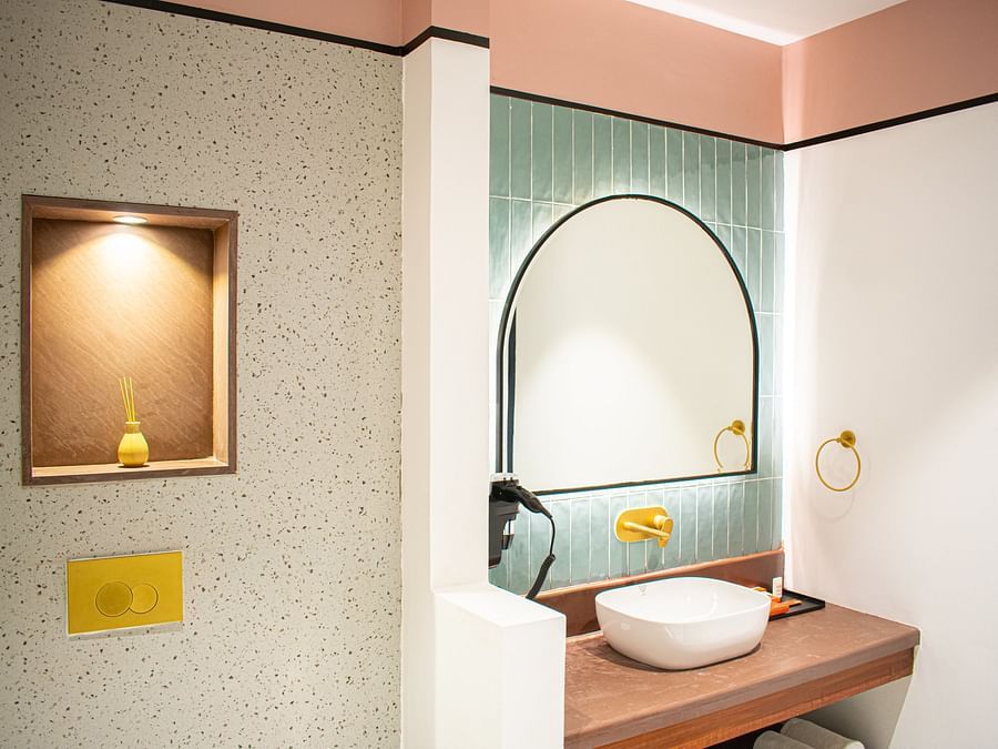 A bathroom with terrazzo walls featuring a round mirror, a basin, and gold fixtures.