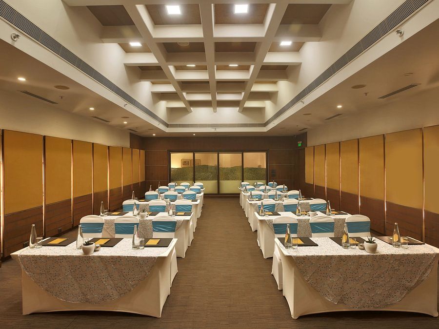 Modern conference room with rows of tables, blue and white chair covers, and a structured ceiling - Heritage Village Resorts & Spa.