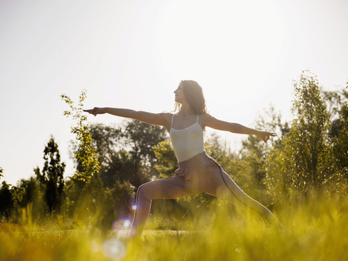 A woman practicing yoga outdoor on a sunny day surrounded by trees
