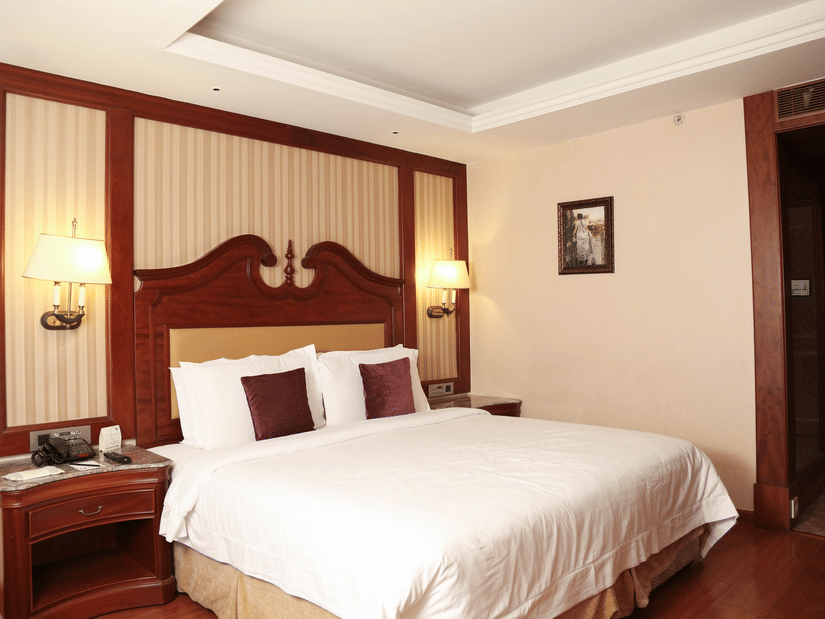Spacious king bedroom with wooden flooring, warm lighting, and elegant interiors for comfortable day stays near Chennai airport | Hablis Hotel Chennai