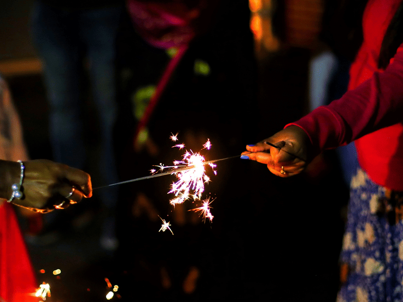 Person lighting a sparkler beside glowing oil lamps during a Diwali celebration in Chennai
