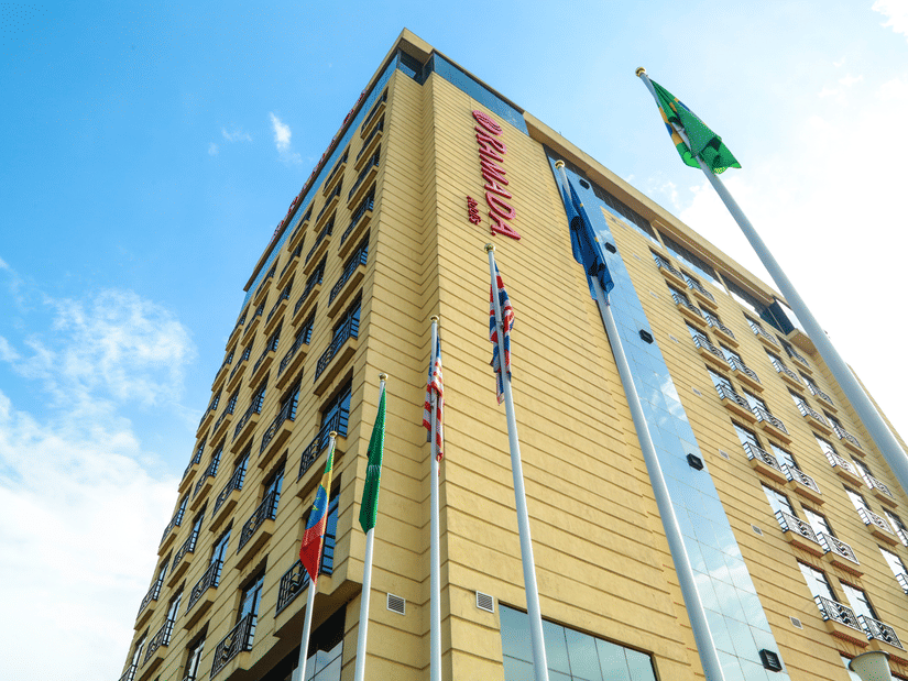 Facade of Ramada by Wyndham Addis, Addis Ababa, with blue sky in the background and flags lined up in front of the building