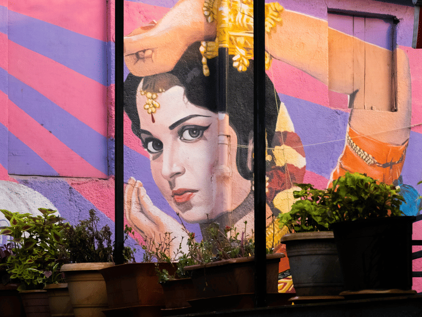 A colourful wall mural depicting a traditional Indian classical dancer with expressive eyes, ornate jewellery, and graceful hand gestures against a vibrant backdrop.