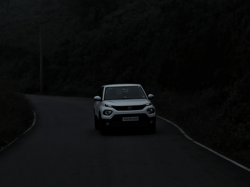 A car driving on an empty street during low visibility time with the roads being lined with trees.
