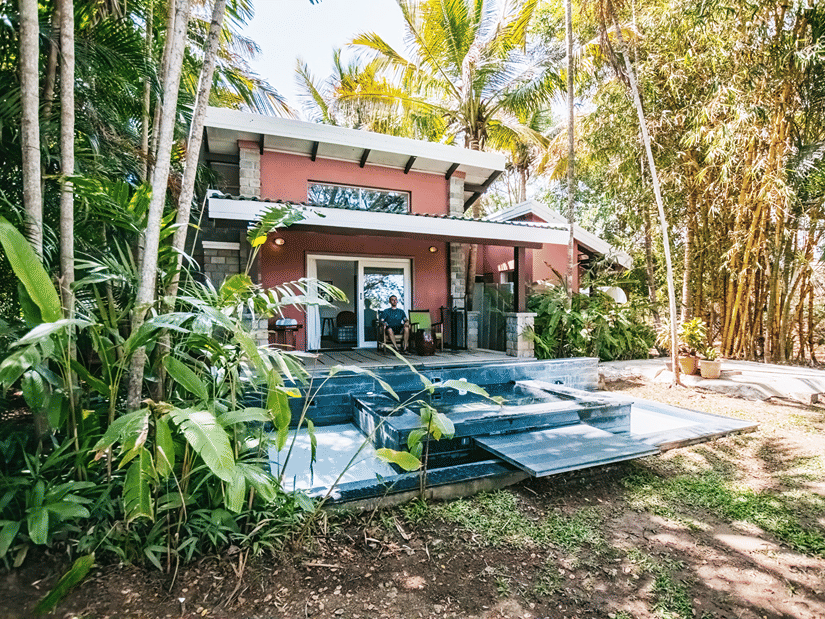 The Residence at Serai Kabini with its red walls and a front deck to relax all while being surrounded by lush green trees and shrubs.