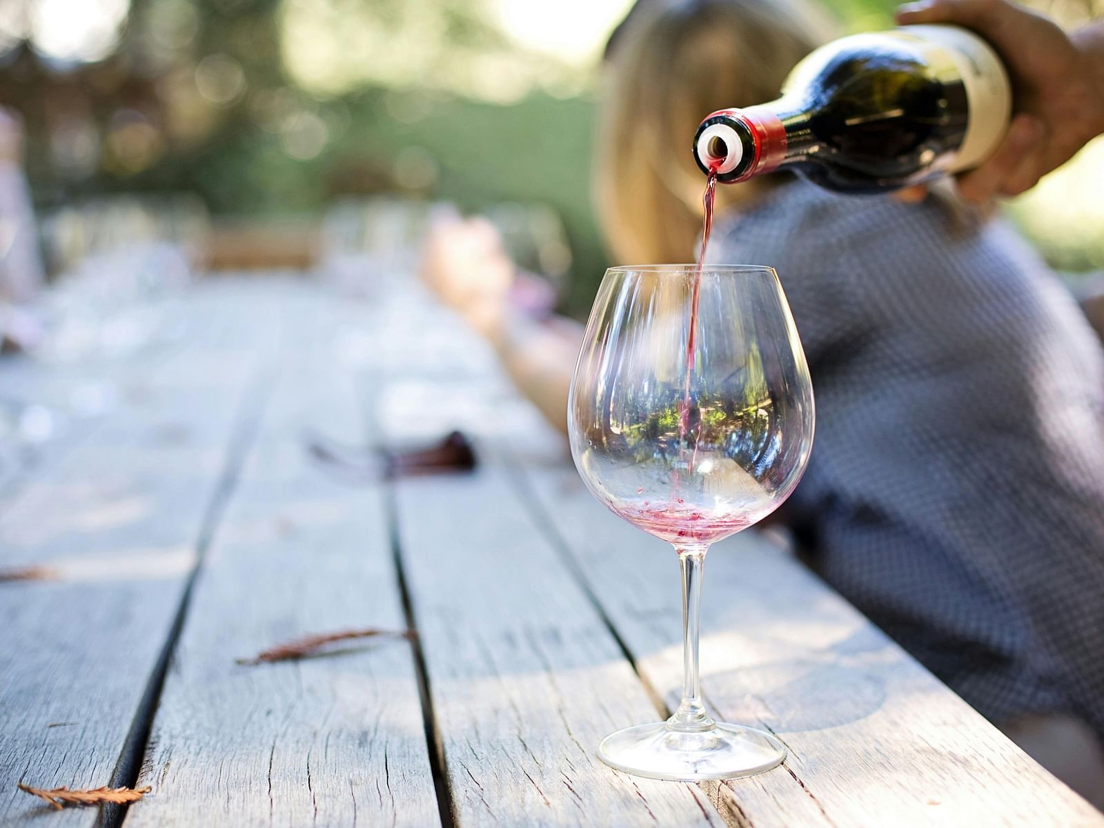 Wine being poured by a staff member into a glass that is kept on a wooden table.