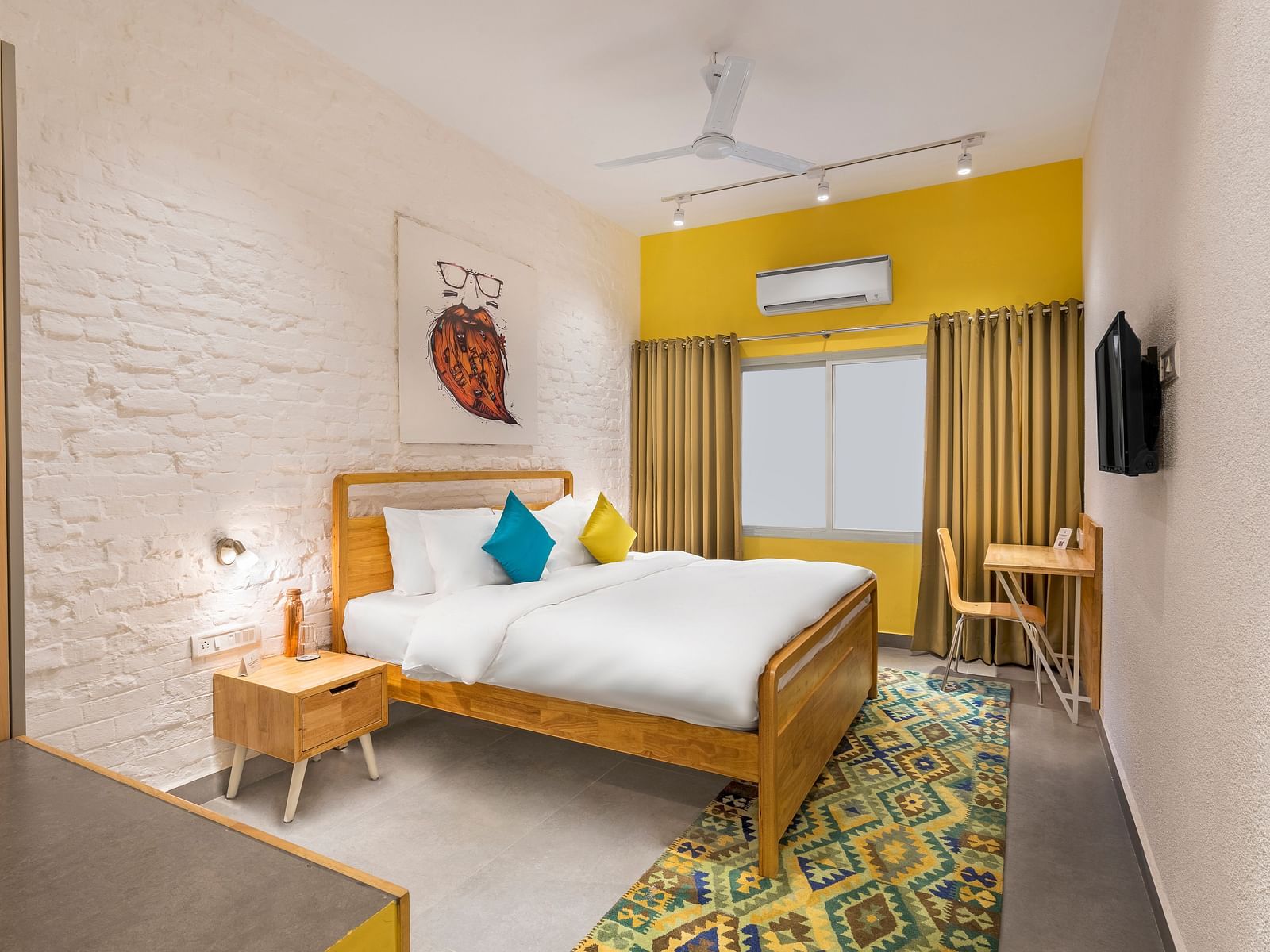 An interior image of the standard room at Bedzzz Varanasi showcases a spacious layout, featuring a comfortable double bed, a cozy floor mat, a stylish study table and chair, a charming coffee table, elegant curtains, an air conditioner for a refreshing amb
