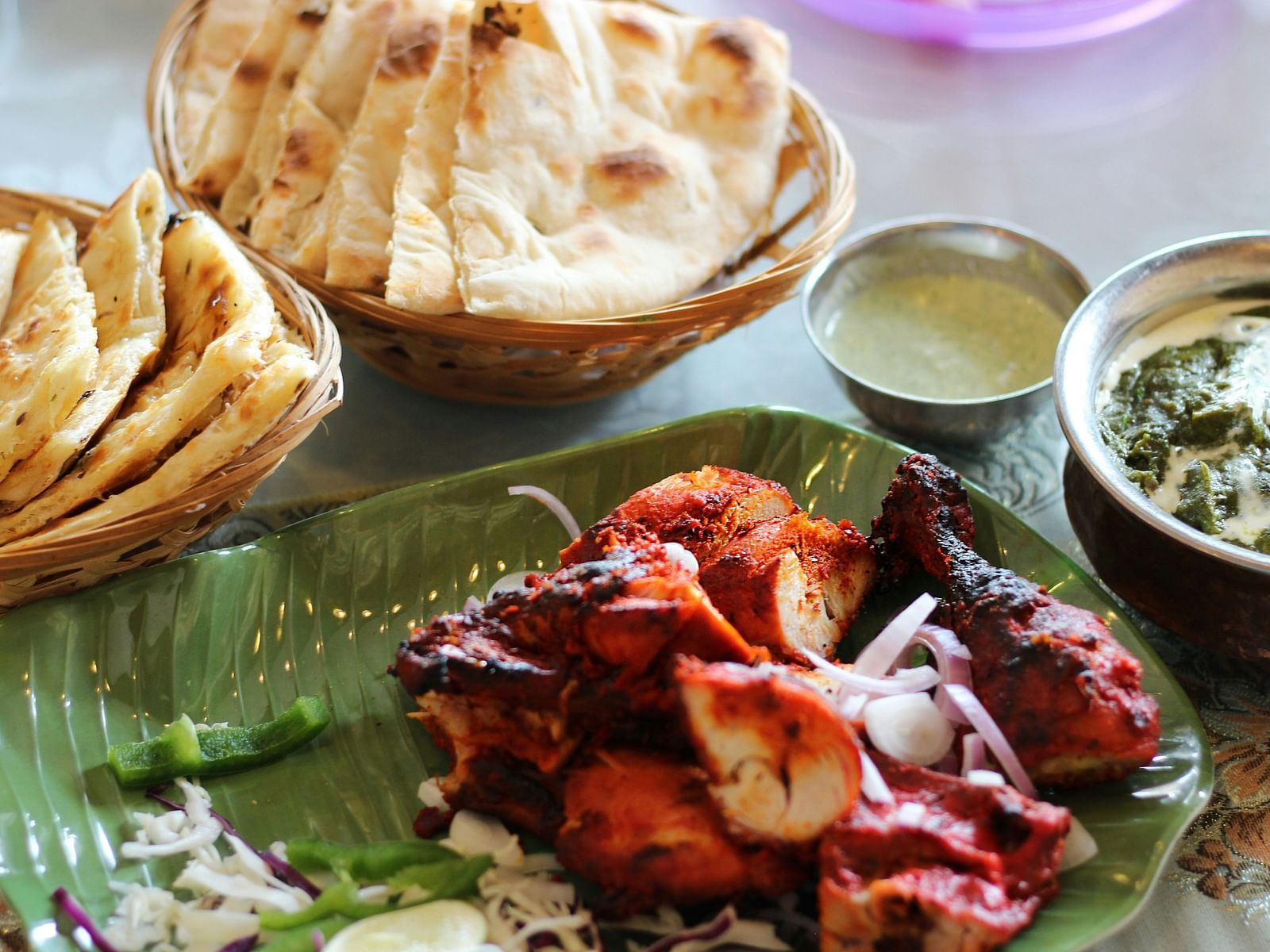 A delicious Indian meal featuring naan, tandoori chicken, green chutney, and a glass of buttermilk served on a traditional plate.